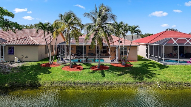 back of property with a lanai, a water view, and a yard