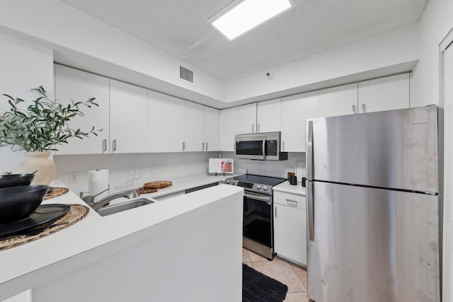 kitchen with a textured ceiling, white cabinetry, appliances with stainless steel finishes, light tile patterned flooring, and sink