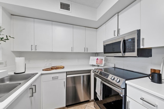 kitchen with light tile patterned floors, appliances with stainless steel finishes, sink, and white cabinetry