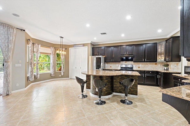 kitchen featuring stainless steel appliances, hanging light fixtures, a center island, light stone countertops, and backsplash