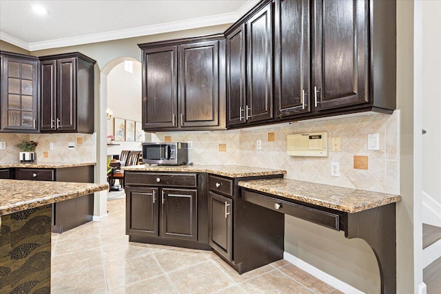 kitchen featuring light stone countertops, light tile patterned floors, ornamental molding, dark brown cabinetry, and backsplash