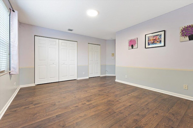 unfurnished bedroom featuring dark hardwood / wood-style flooring and two closets