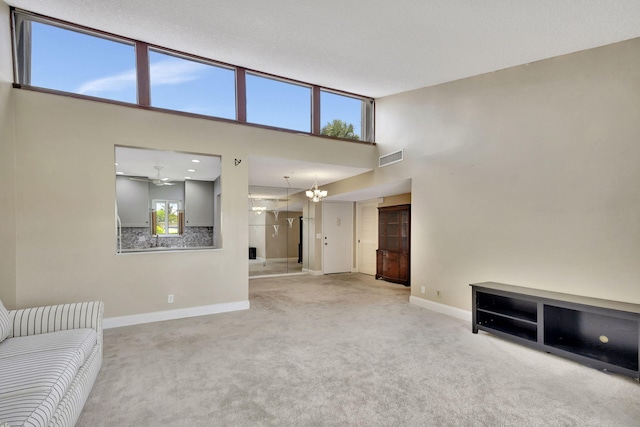 unfurnished living room featuring carpet, a towering ceiling, and ceiling fan with notable chandelier