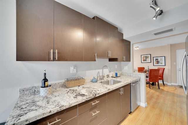 kitchen with light hardwood / wood-style floors, dark brown cabinets, stainless steel dishwasher, light stone counters, and sink