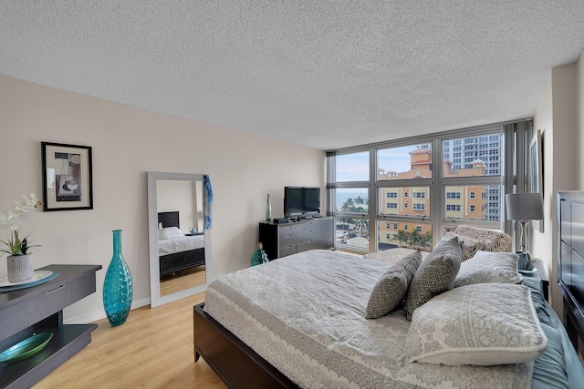 bedroom with a wall of windows, a textured ceiling, and light hardwood / wood-style floors