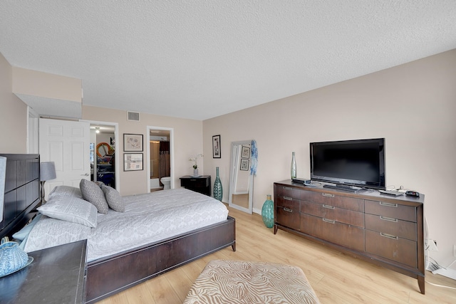 bedroom with connected bathroom, light wood-type flooring, a spacious closet, and a textured ceiling