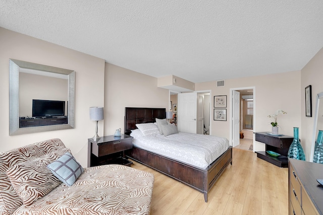 bedroom with a textured ceiling, light hardwood / wood-style flooring, and connected bathroom