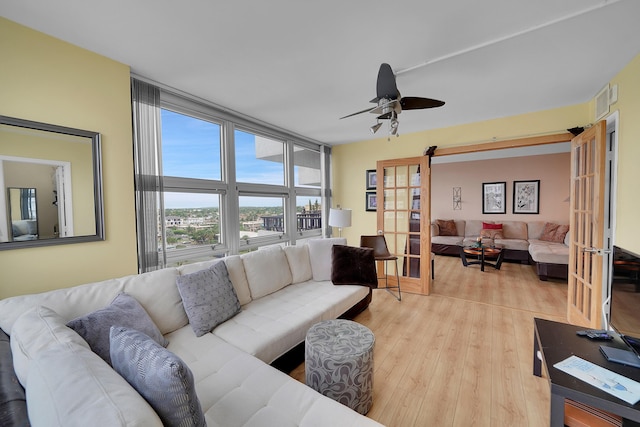 living room featuring ceiling fan, a wall of windows, french doors, and light hardwood / wood-style floors