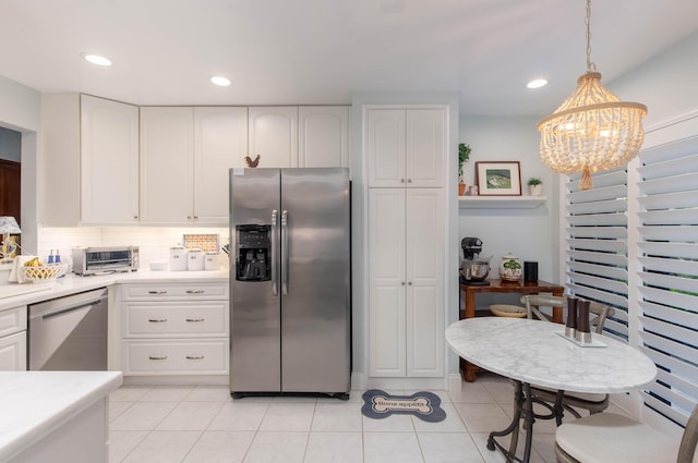 kitchen featuring light tile patterned floors, appliances with stainless steel finishes, white cabinetry, backsplash, and decorative light fixtures