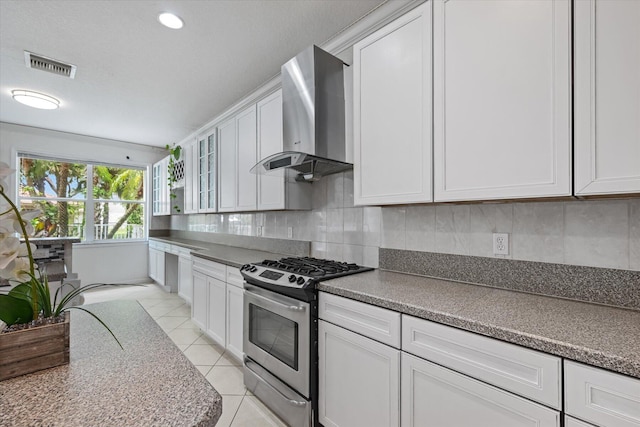 kitchen with white cabinets, wall chimney range hood, backsplash, gas range, and light tile patterned flooring