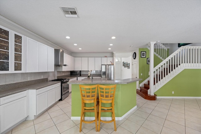 kitchen with white cabinets, stainless steel appliances, a center island with sink, and wall chimney range hood