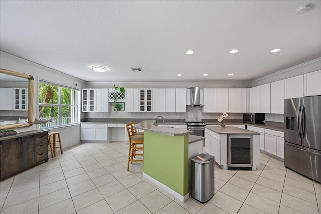 kitchen with wall chimney range hood, white cabinets, a center island, a breakfast bar, and appliances with stainless steel finishes