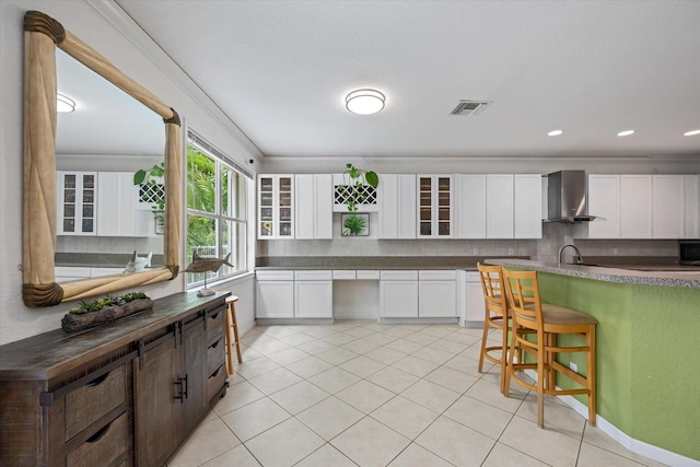 kitchen featuring ornamental molding, white cabinetry, and wall chimney range hood