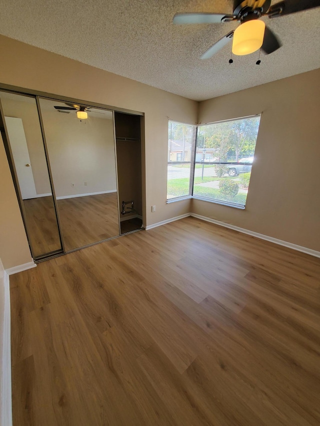 unfurnished bedroom with a textured ceiling, ceiling fan, a closet, and hardwood / wood-style floors