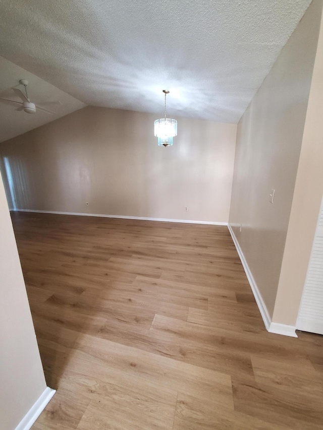 empty room featuring a textured ceiling, lofted ceiling, ceiling fan with notable chandelier, and light wood-type flooring