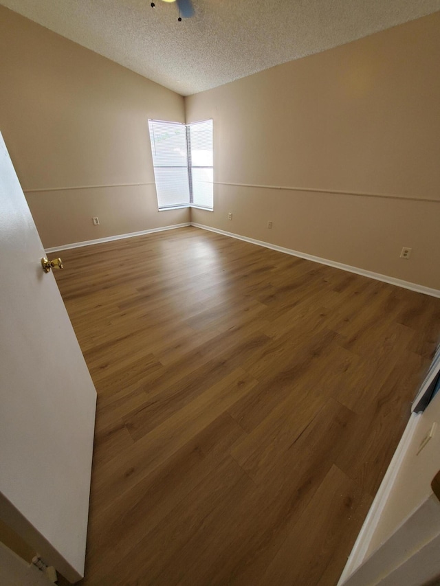 unfurnished room with vaulted ceiling, a textured ceiling, and hardwood / wood-style flooring