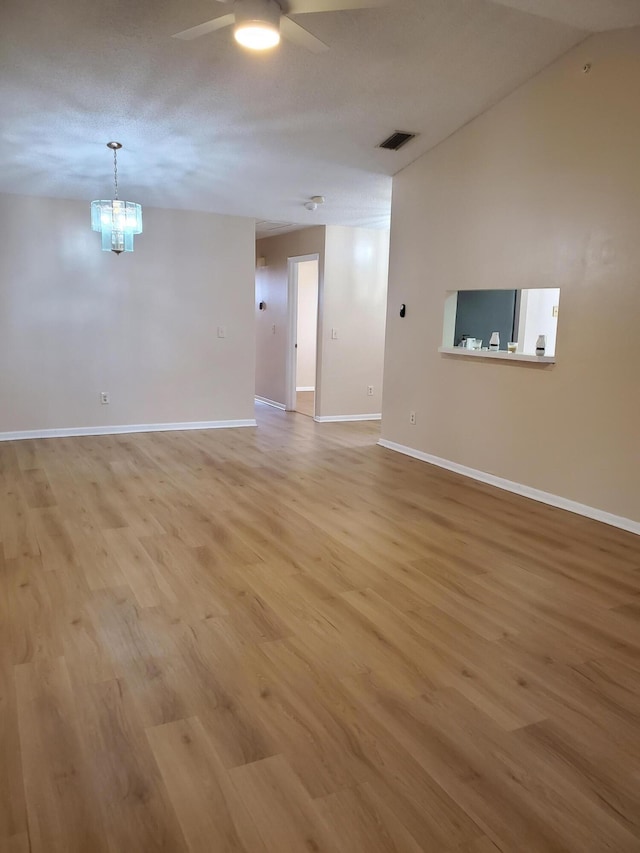 empty room featuring ceiling fan with notable chandelier, a textured ceiling, and light hardwood / wood-style flooring