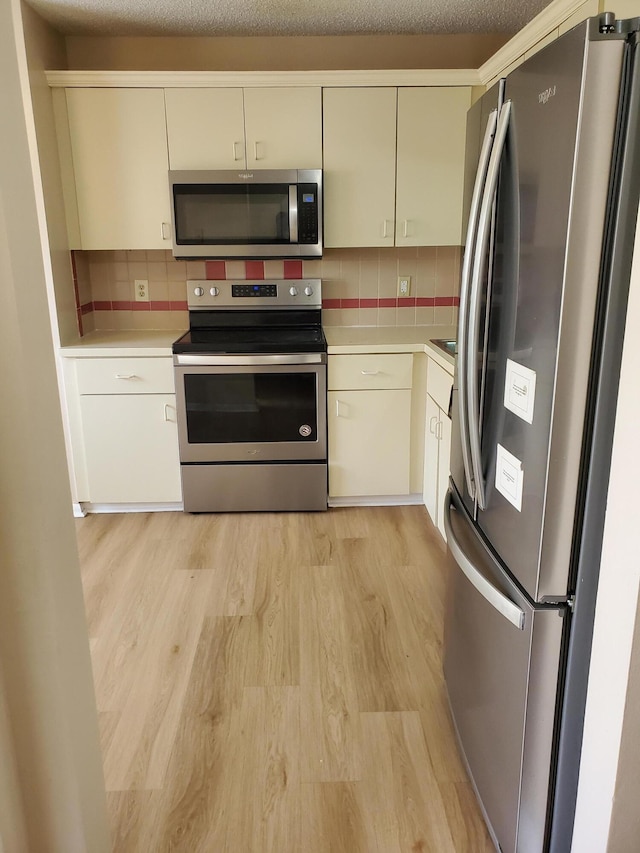 kitchen with decorative backsplash, light hardwood / wood-style flooring, a textured ceiling, stainless steel appliances, and cream cabinets