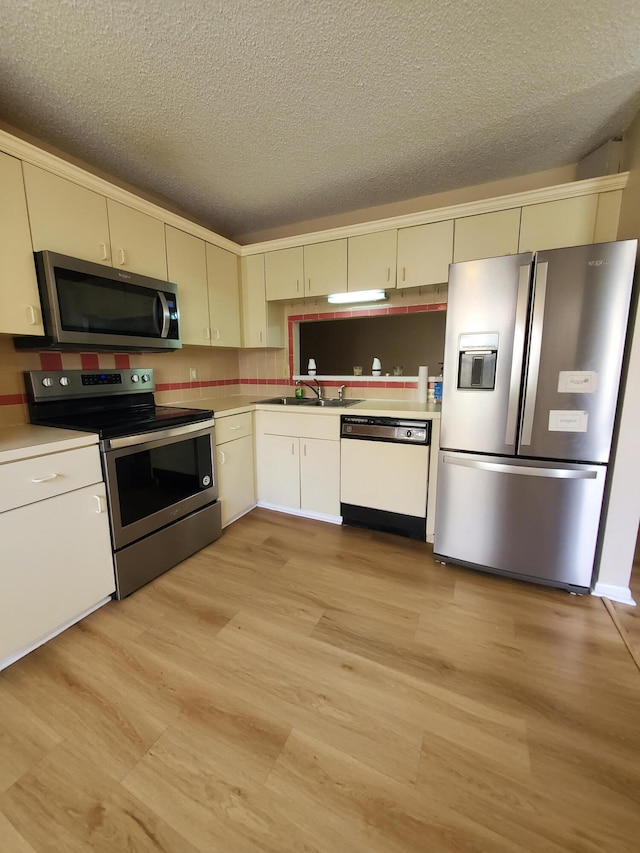 kitchen with a textured ceiling, stainless steel appliances, cream cabinets, and sink