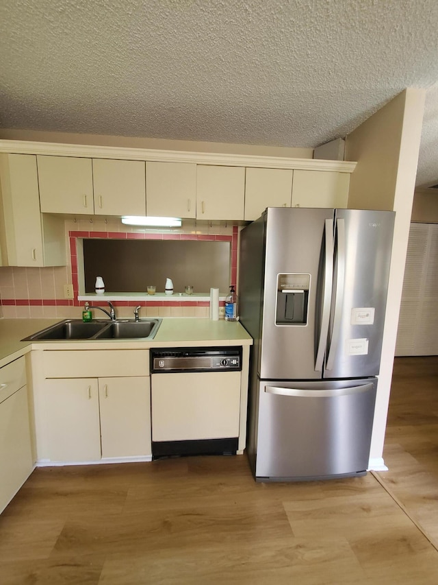 kitchen with a textured ceiling, sink, stainless steel fridge, cream cabinets, and white dishwasher