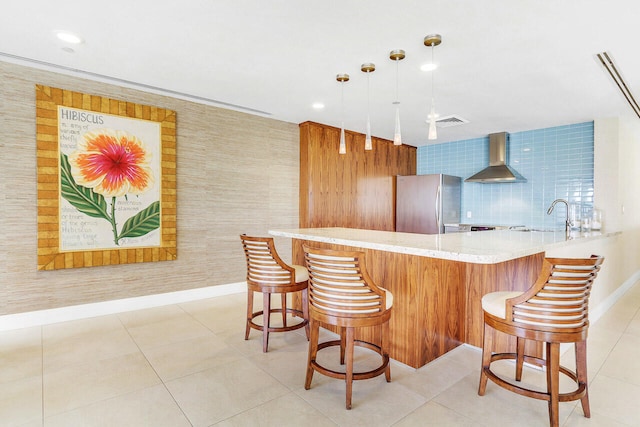 kitchen with pendant lighting, kitchen peninsula, sink, stainless steel refrigerator, and wall chimney exhaust hood