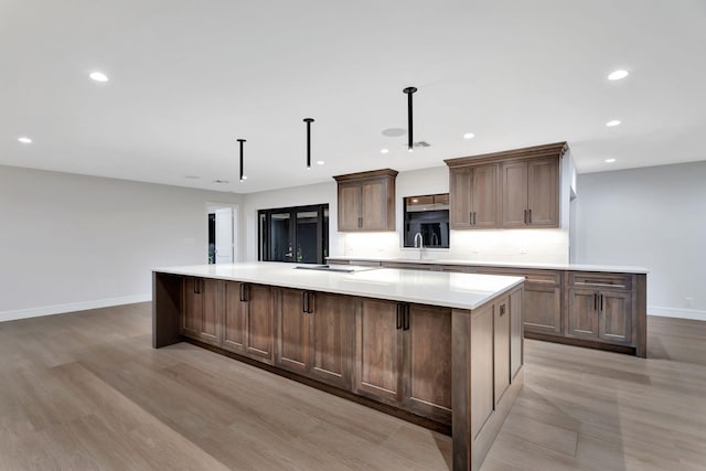 kitchen with stovetop, light hardwood / wood-style flooring, sink, pendant lighting, and a large island