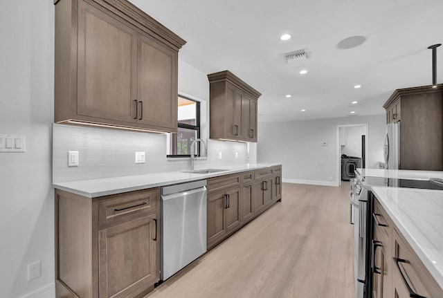 kitchen with decorative backsplash, sink, stainless steel appliances, and light hardwood / wood-style flooring