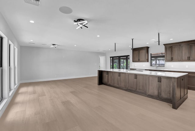 kitchen featuring light wood-type flooring, dark brown cabinets, a center island, and backsplash