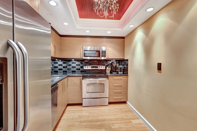 kitchen featuring light brown cabinets, light wood-type flooring, stainless steel appliances, decorative backsplash, and a raised ceiling