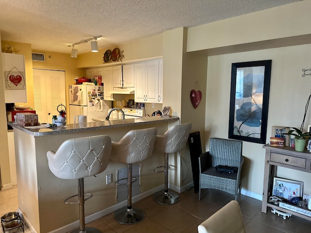 kitchen with white cabinetry, white refrigerator, rail lighting, a textured ceiling, and tile patterned flooring