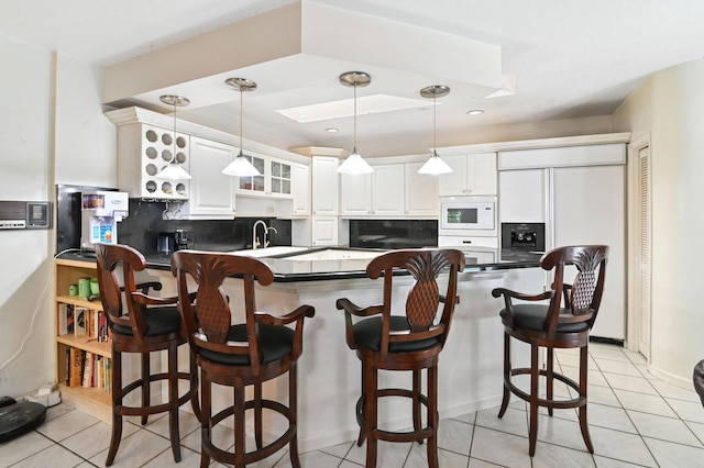 kitchen featuring kitchen peninsula, light tile patterned floors, white cabinetry, a kitchen bar, and built in appliances