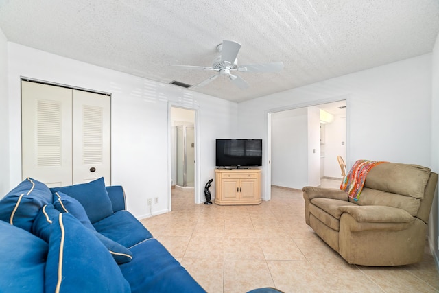 living room with ceiling fan, a textured ceiling, and light tile patterned flooring