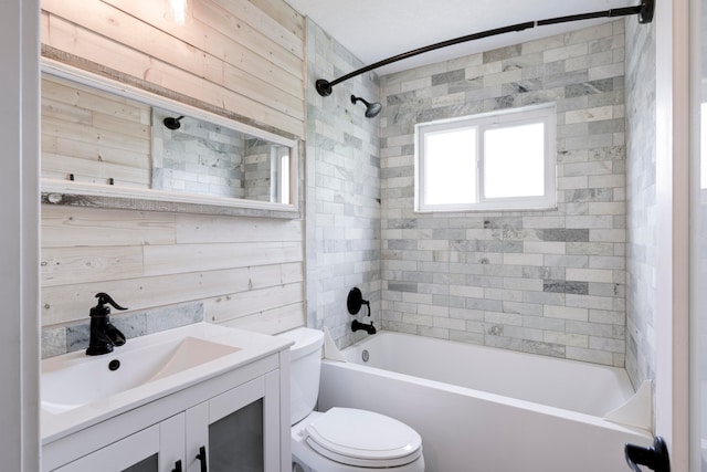 full bathroom featuring wooden walls, vanity, tiled shower / bath, and toilet