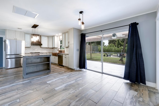 kitchen with appliances with stainless steel finishes, wall chimney range hood, backsplash, decorative light fixtures, and a center island