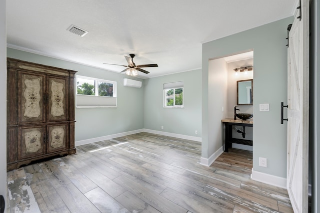 unfurnished bedroom featuring a wall unit AC, multiple windows, light hardwood / wood-style flooring, and ceiling fan