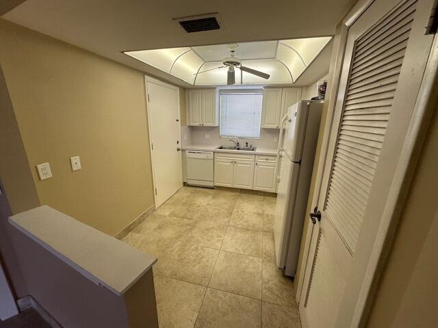 kitchen featuring a tray ceiling, light countertops, visible vents, a sink, and white appliances