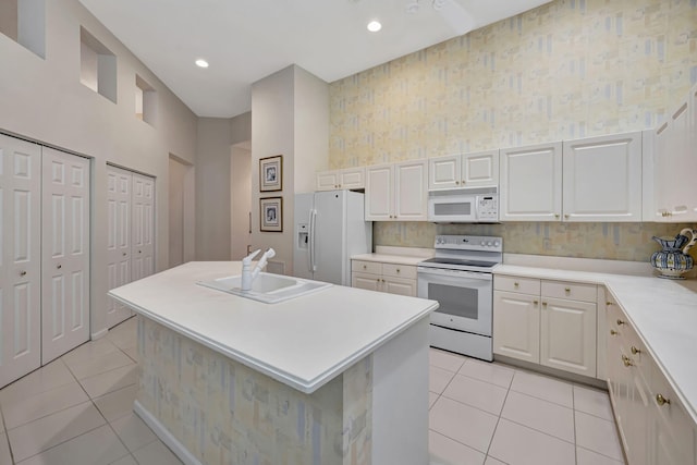 kitchen featuring light tile patterned floors, white appliances, a center island with sink, and sink