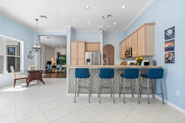 kitchen with kitchen peninsula, appliances with stainless steel finishes, light brown cabinets, a breakfast bar area, and ornamental molding