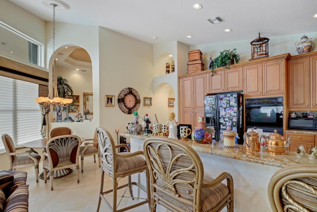 kitchen with light stone countertops, a breakfast bar, black appliances, light tile patterned floors, and a high ceiling