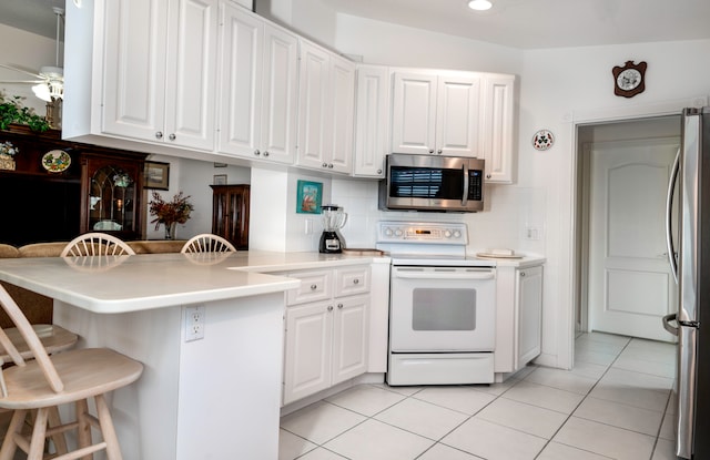 kitchen featuring light tile patterned flooring, white cabinets, backsplash, appliances with stainless steel finishes, and a kitchen bar