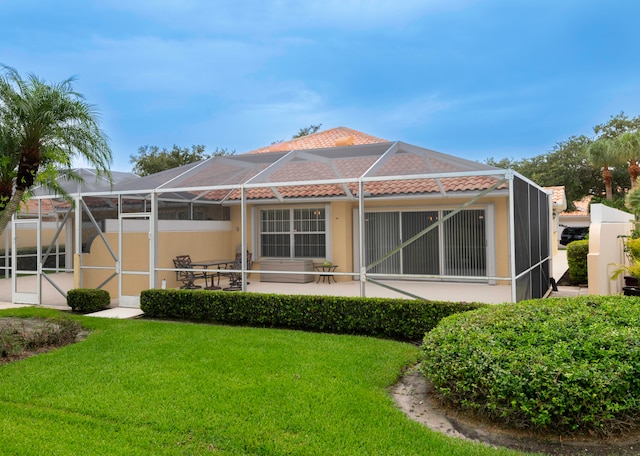 rear view of property featuring a patio, a yard, and glass enclosure