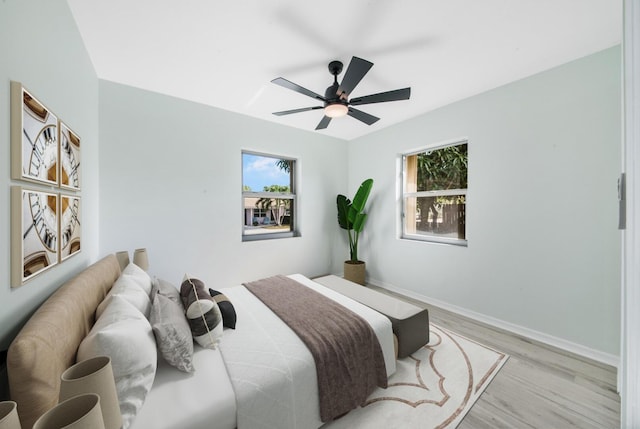 bedroom featuring ceiling fan, light hardwood / wood-style floors, and multiple windows