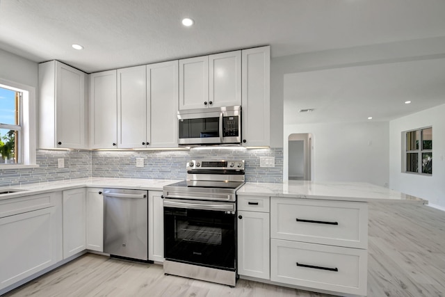 kitchen with white cabinetry, kitchen peninsula, appliances with stainless steel finishes, and light hardwood / wood-style flooring