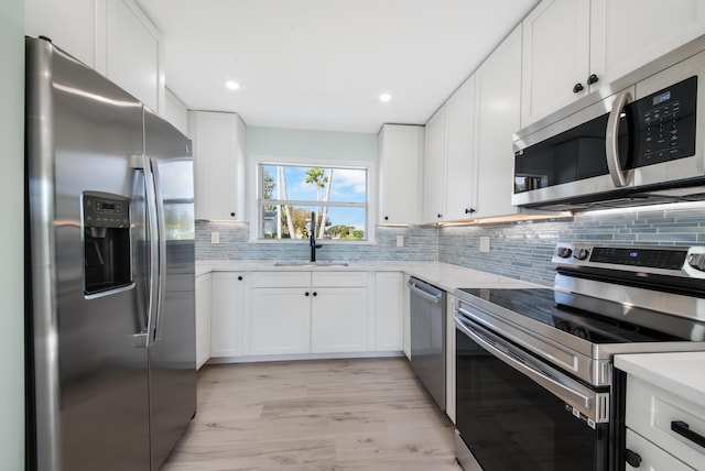 kitchen with decorative backsplash, white cabinetry, light hardwood / wood-style flooring, and stainless steel appliances