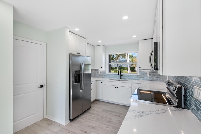 kitchen with appliances with stainless steel finishes, light stone counters, sink, light hardwood / wood-style flooring, and white cabinets