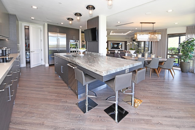 kitchen with a kitchen island with sink, dark brown cabinets, wood-type flooring, stainless steel appliances, and a kitchen bar