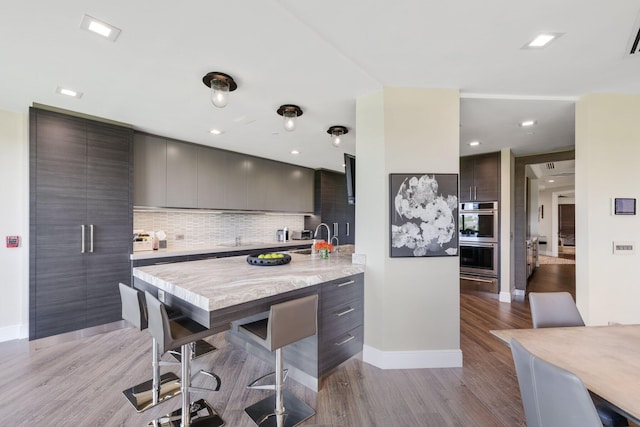 kitchen featuring tasteful backsplash, sink, light wood-type flooring, double oven, and dark brown cabinetry