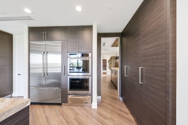 kitchen featuring appliances with stainless steel finishes, light hardwood / wood-style flooring, and dark brown cabinets