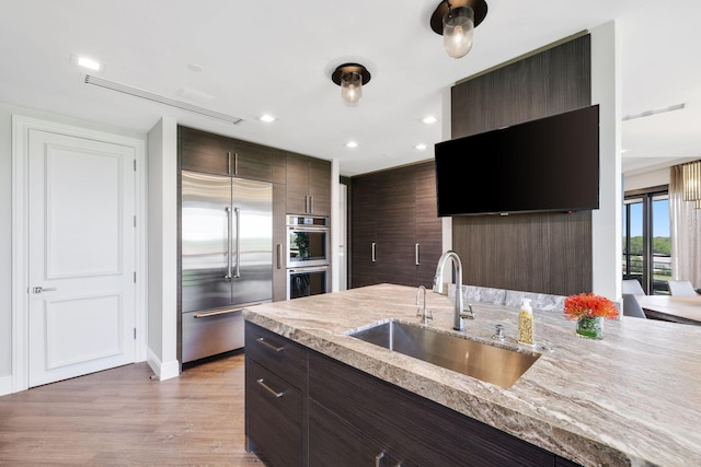 kitchen featuring sink, dark brown cabinetry, light wood-type flooring, appliances with stainless steel finishes, and light stone counters