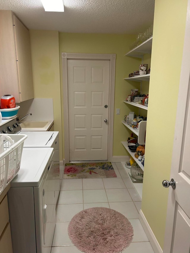 clothes washing area with a textured ceiling, washing machine and dryer, light tile patterned floors, and cabinets